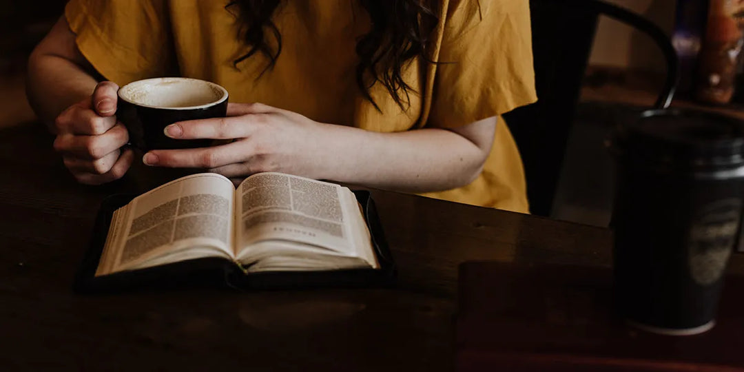 a Woman sitting at a table with coffee, reading a book
